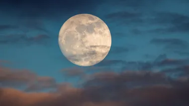 Full moon in a twilight sky surrounded by thin clouds.