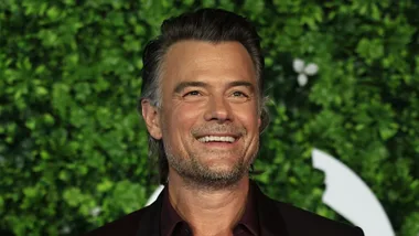 josh duhamel smiling against a leafy background