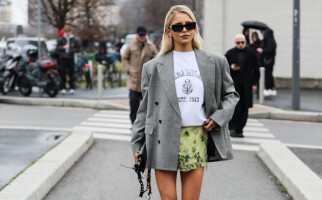 woman wearing a grey blazer, green skirt, white shirt, and black sunglasses