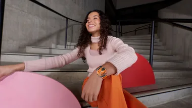 Girl in pink sweater sitting on steps, smiling, wearing an orange wristwatch.