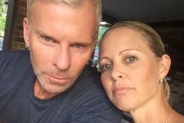 Two individuals taking a selfie indoors, with neutral expressions and a blurred background.