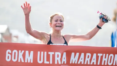 Runner crosses the finish line of a 60km ultra marathon, smiling with arms raised in celebration.